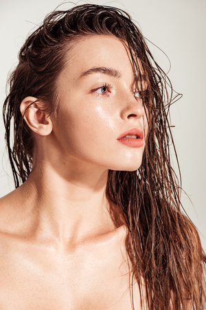 beautiful young woman with coral lips and wet hair looking away isolated on greyの写真素材