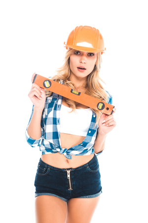 blonde architect woman in blue shirt, shorts and orange hardhat with spirit level isolated on whiteの写真素材