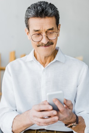 cheerful senior man in glasses looking at smartphone at homeの写真素材