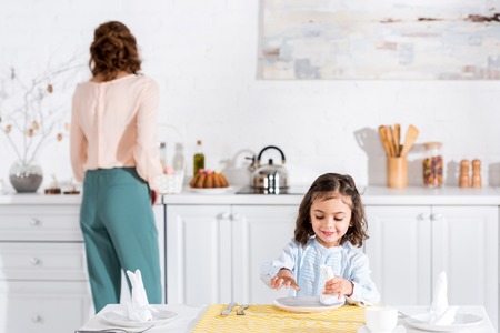 Smiling preschooler kid folding napkin at table in kitchen