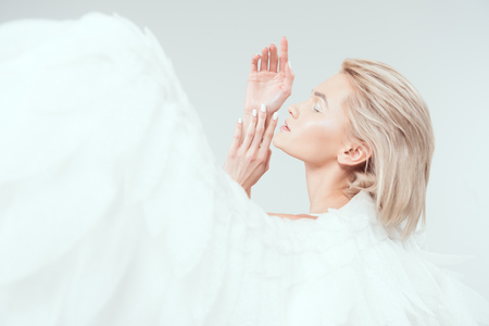 selective focus of beautiful tender woman with angel wings gesturing with hands isolated on whiteの写真素材