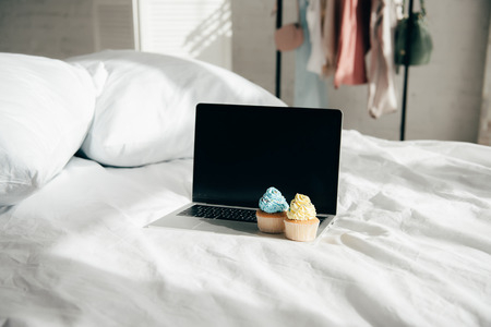 sweet and tasty cupcakes on laptop with blank screen in bedroomの写真素材