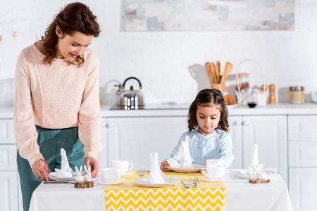Mother and little daughter serving table with napkins in kitchenの写真素材