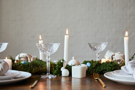 crystal glasses, burning candles, green moss and  quail eggs on napkin and dishware table at home