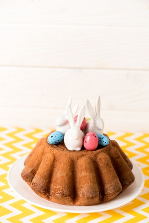 Easter bread with painted quail eggs and ceramic rabbits on yellow surface