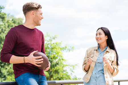 cheerful young woman looking at man with american football in handsの写真素材