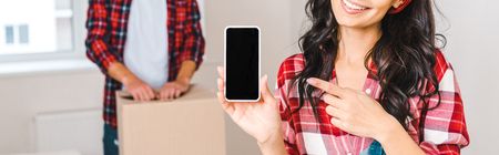 cropped view of happy woman pointing with finger at smartphone with blank screen near man at home