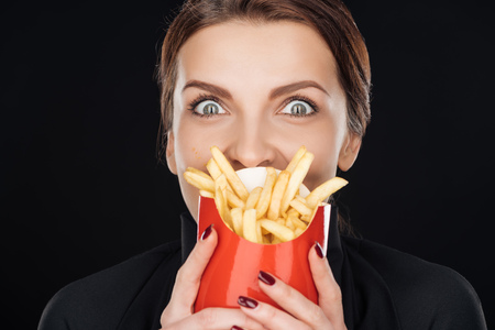 shocked woman covering face with french fries isolated on blackの写真素材