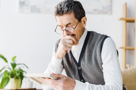 retired man in glasses crying while looking at photo at homeの写真素材