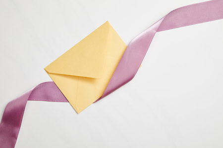 top view of yellow envelope and violet satin ribbon on whiteの写真素材