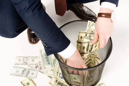 cropped view of businessman taking dollar banknotes from trash can on whiteの写真素材