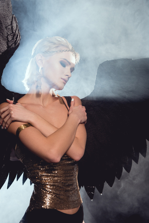 beautiful young sexy woman with black angel wings posing on smoky backgroundの写真素材