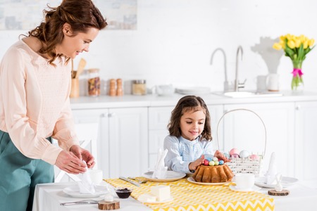 Smiling kid looking at easter cake while mother folding napkinsの写真素材