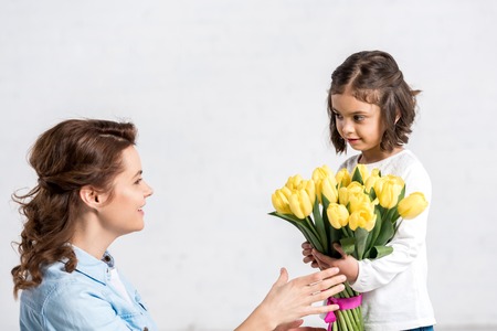 Smiling mother sniffing yellow tulips from daughter isolated on whiteの写真素材