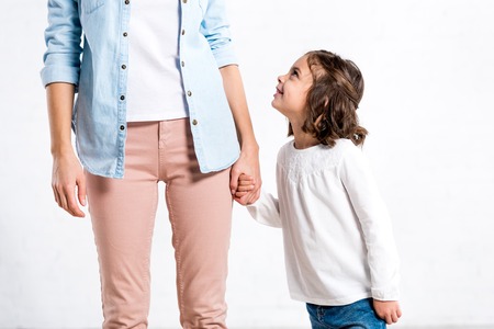 Partial view of woman in blue shirt holding hands with daughter on white