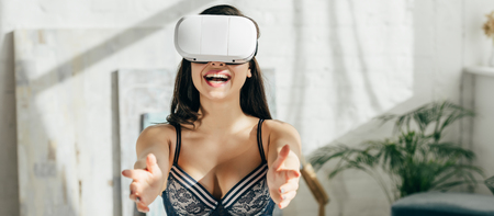 panoramic shot of happy brunette woman in underwear wearing virtual reality headset