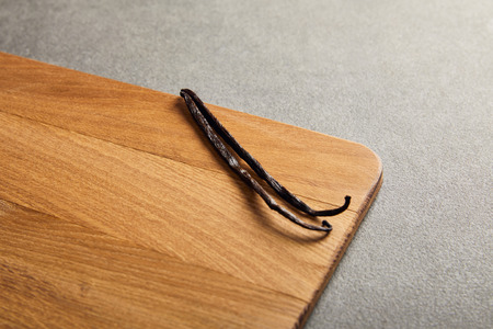 Vanilla pods lying on wooden cutting board on dark surfaceの写真素材