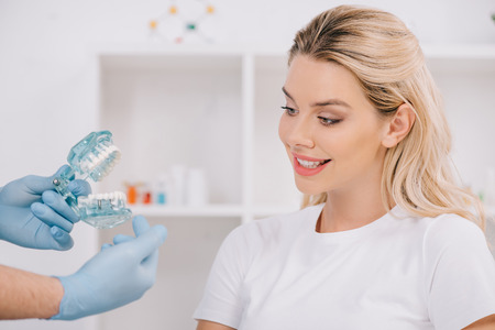 beautiful smiling woman looking at orthodontist holding jaw model during consultation in clinic