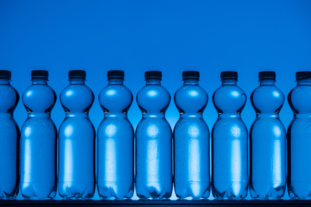 toned image of plastic water bottles on neon blue background with backlitの写真素材