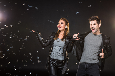 beautiful happy couple in leather jackets cheering with falling confetti on black backgroundの写真素材