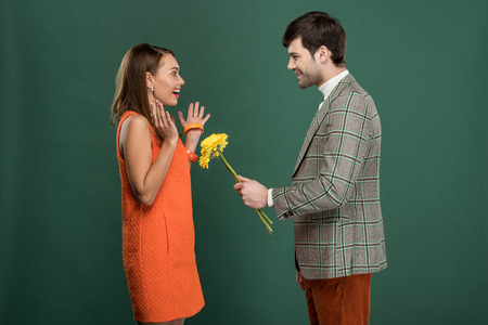 handsome man in vintage clothes presenting flowers to beautiful happy woman isolated on green