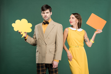 beautiful couple in vintage clothes holding speech bubble and thought bubble isolated on greenの写真素材