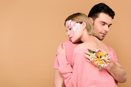 handsome man with alstroemeria flowers on hand embracing girlfriend with flowers on face isolated on...