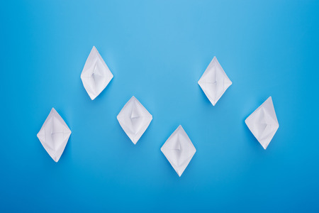 Flat lay with white paper boats on blue surface