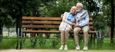 happy senior couple hugging while sitting on wooden bench in parkの写真素材