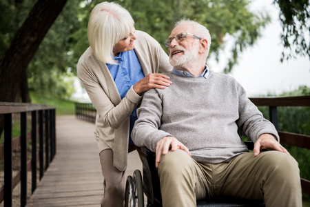 nice senior woman with husband in wheelchair in parkの写真素材