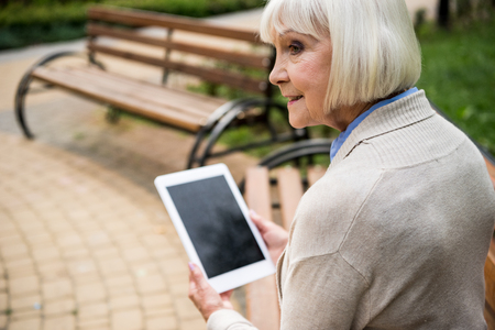 selective focus of senior woman using digital tablet while sitting on wooden benchの写真素材