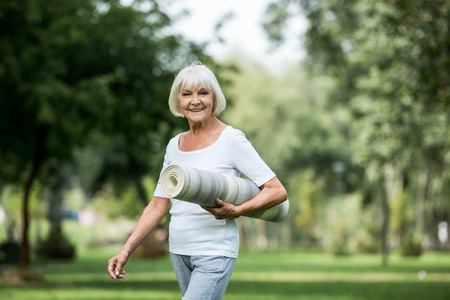 happy senior woman with fitness mat walking in parkの写真素材
