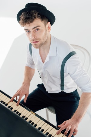 dreamy pianist in white shirt and black hat playing piano