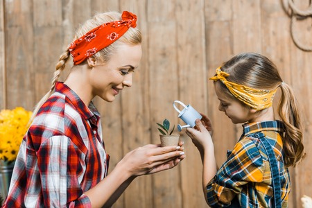 mother holding small plant while daughter watering with toy watering canの写真素材