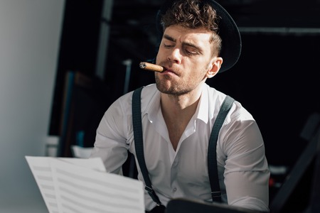 handsome musician holding music book sheets while smoking cigarの写真素材