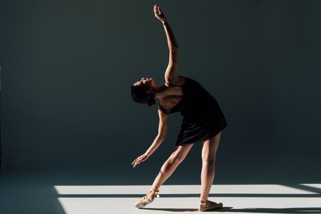 graceful young ballerina in black dress dancing in sunlightの写真素材