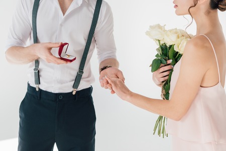 cropped view of man making marriage proposal to girl with bouquet of roses
