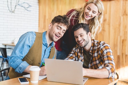 handsome and beautiful friends using laptop and smiling at cafe
