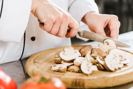 partial view of female chef cutting mushrooms in restaurant kitchenの写真素材