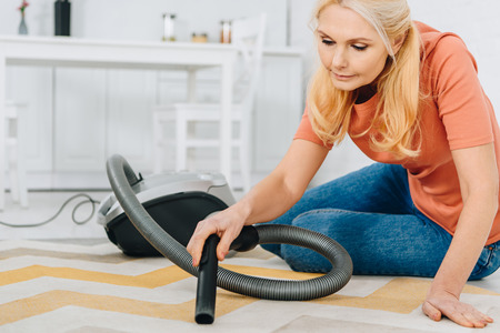 Concentrated blonde woman in jeans using vacuum cleanerの写真素材