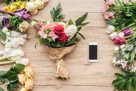 Fresh flowers and smartphone with blank screen on wooden surfaceの写真素材