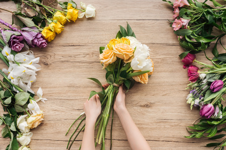Partial view of florist holding bouquet of fresh flowers on wooden surfaceの写真素材