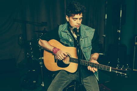 stylish and handsome singer playing acoustic guitar near microphoneの写真素材