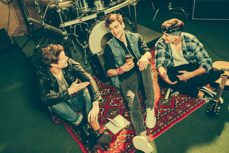 overhead view of happy rock band talking while sitting on carpet near musical instruments