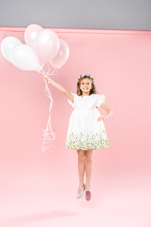 carefree child jumping with white and pink air balloons on bicolor backgroundの写真素材
