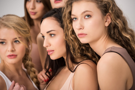 selective focus of attractive women standing together while support each other isolated on greyの写真素材