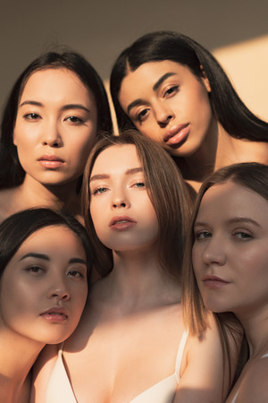 five attractive multicultural young women looking at camera in sunlight