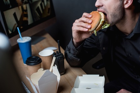 cropped view of guard eating burger at workplaceの写真素材