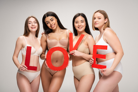 four beautiful multiethnic girls in underwear holding paper cut word "love" isolated on grey, body positivity conceptの写真素材
