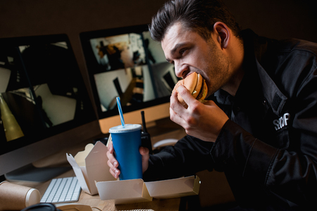 guard eating burger and holding paper cup at workplaceの写真素材